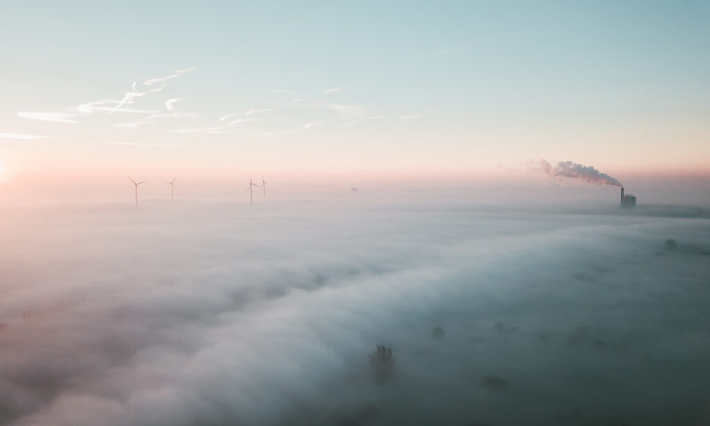 A layer of fog over a field with wind turbines and a factory