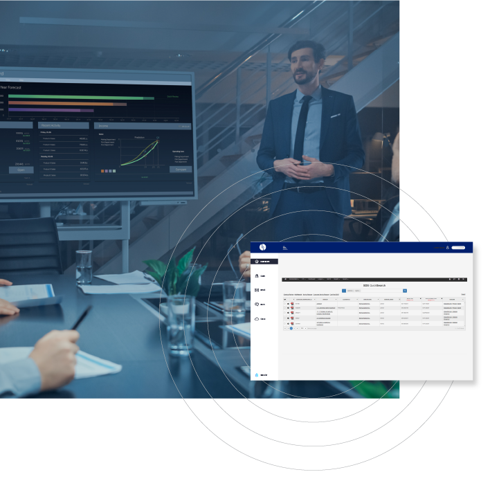 Indoor shot of a business meeting with an interactive display showing performance data, a presenter in a suit, and a Sphera’s dashboard SDS Management Software interface on a monitor.