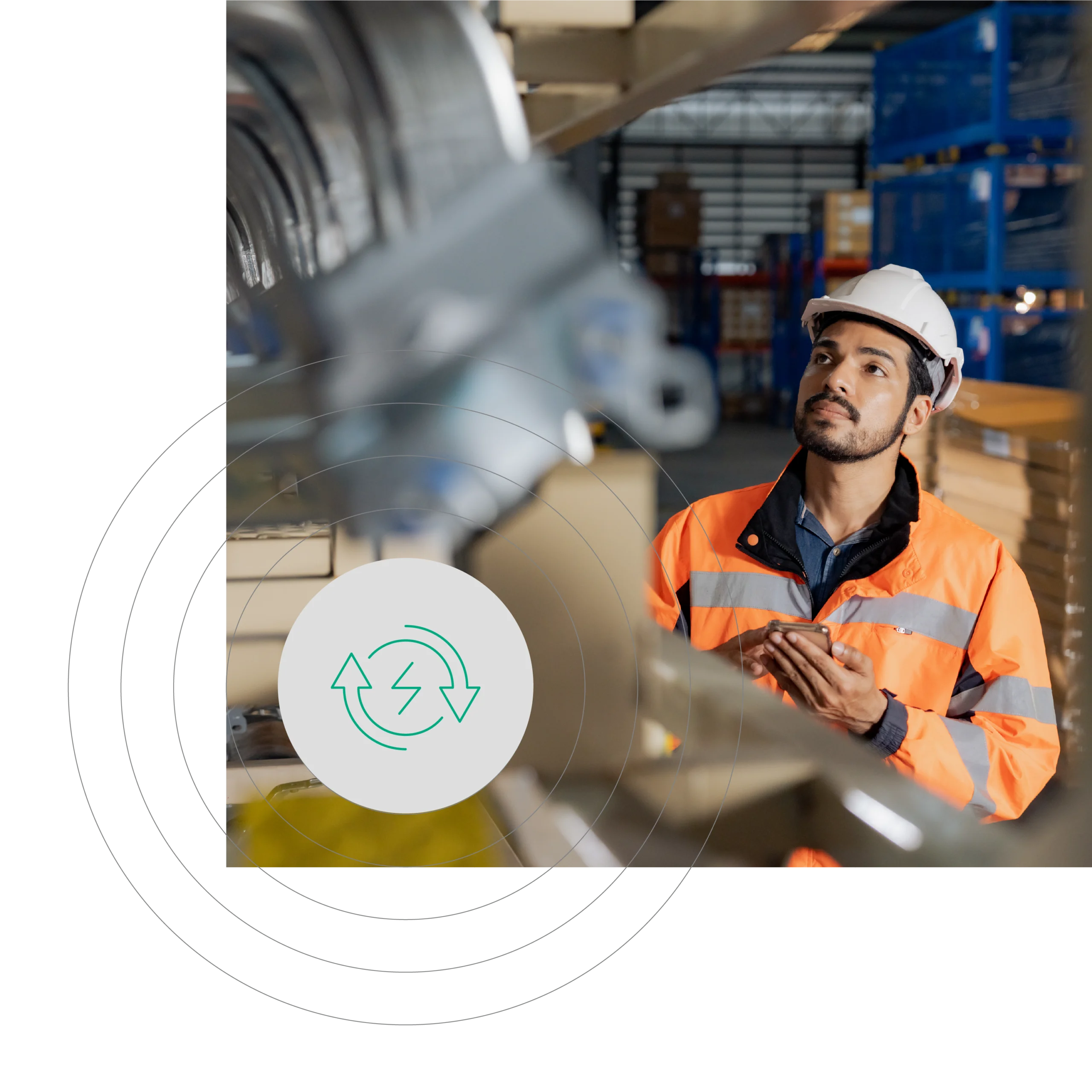 Indoor shot of a South Asian man in an orange safety vest and white helmet inspecting equipment in a warehouse. Background shows machinery and shelving units.